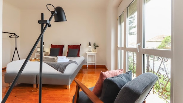 A bedroom with a bed, bedside table, lamp, and a view of the outdoors through large windows. - Belem Boutique Viii by Homing (Lisbon)