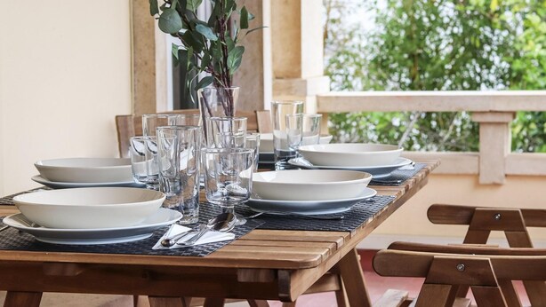 A wooden dining table set with white plates, clear glasses, and a vase with green leaves. - Belem Boutique V by Homing (Lisbon)