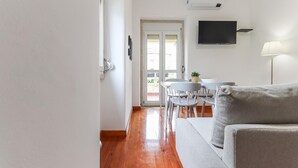 A modern living room with a sofa, a TV mounted on the wall, and a dining area with a table and chairs. - Belem Boutique V by Homing (Lisbon)