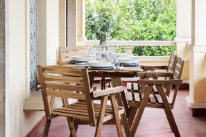 A wooden table set with plates, glasses, and a vase, positioned near a window with a view of greenery. - Belem Boutique V by Homing (Lisbon)