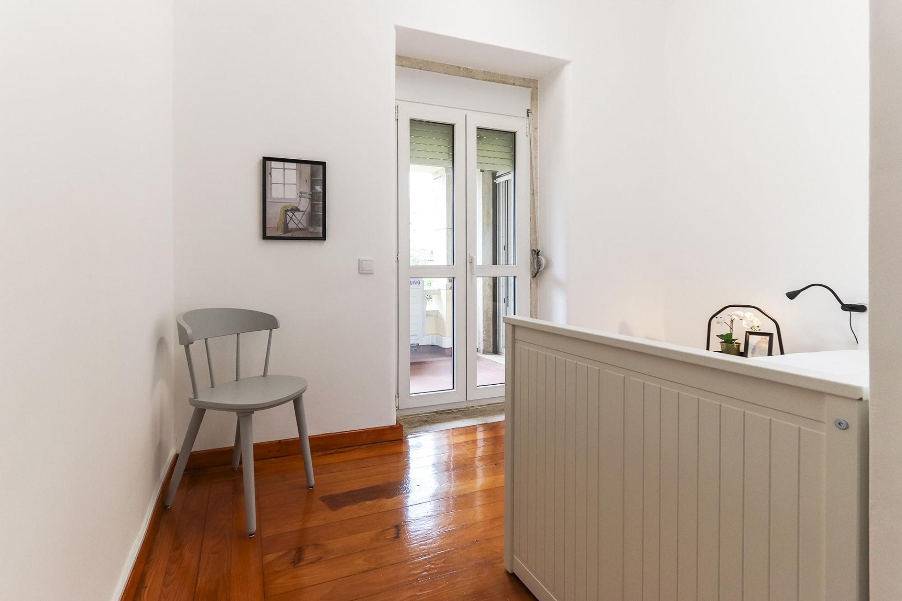 A room with a wooden floor, a white radiator, a chair, and a door leading to an outdoor area.