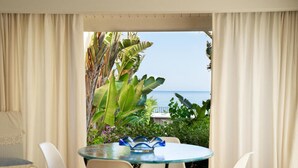 Una stanza con tavolo e sedie in vetro, vista sul mare e piante tropicali.