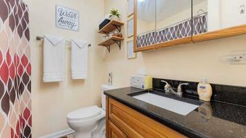 Ein Badezimmer mit Waschbecken, Spiegel und Toilette. Handtücher und ein Handtuchhalter, eine Duschvorhang und ein Schild mit der Aufschrift 'Wash Away'.