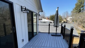 Una terraza de madera con barandilla negra, un portón corredera de vidrio y un parasol.