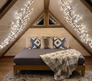 A cozy attic bedroom with a wooden bed, patterned pillows, and string lights.