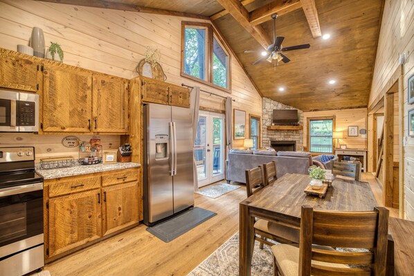 A wooden cabin interior with a kitchen, dining area, and a stone fireplace.