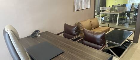 Una sala de conferencias con una mesa de madera, sillas de cuero y una computadora portátil.