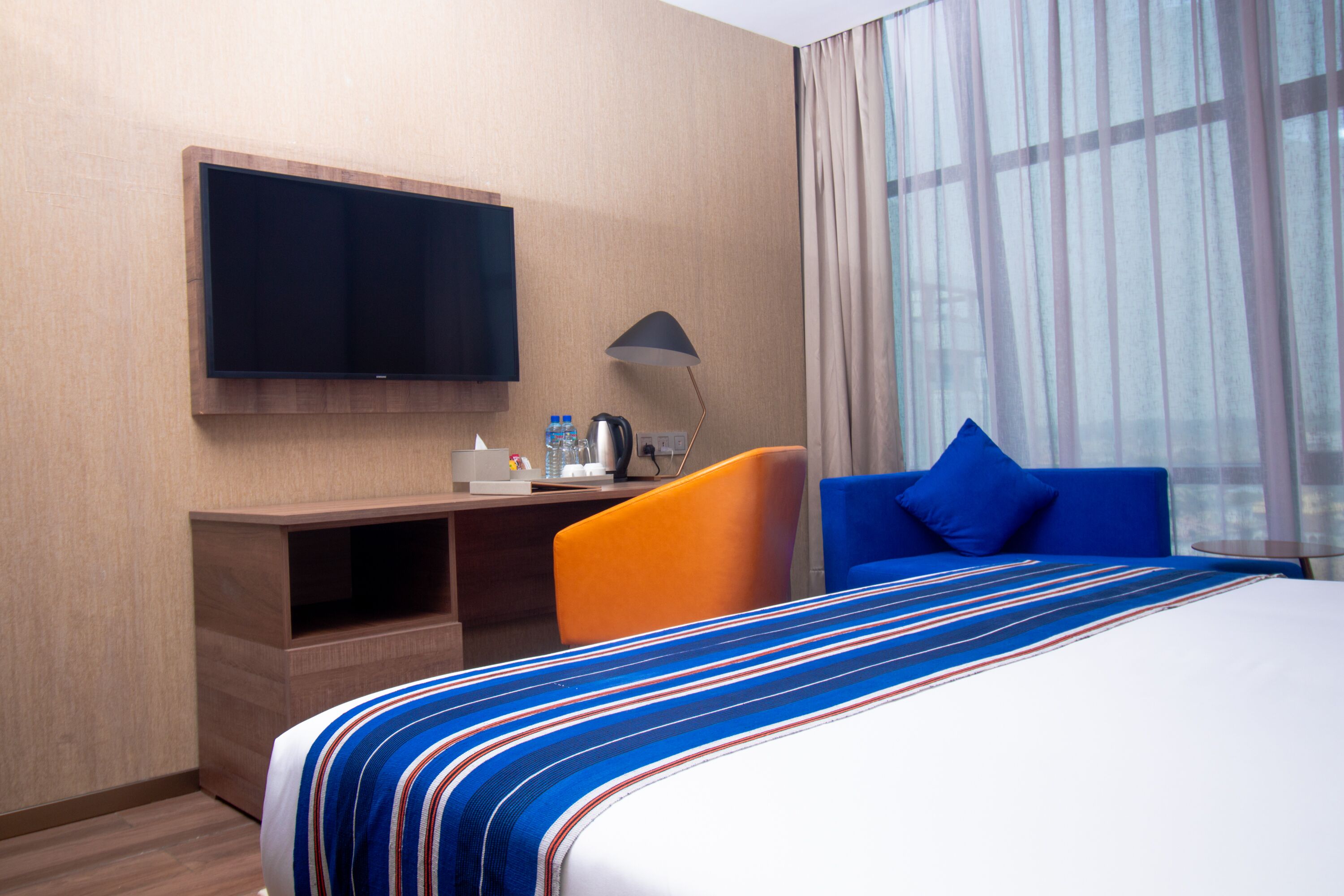 A hotel room with a bed, a desk, a chair, a television, a lamp, and a window with curtains.