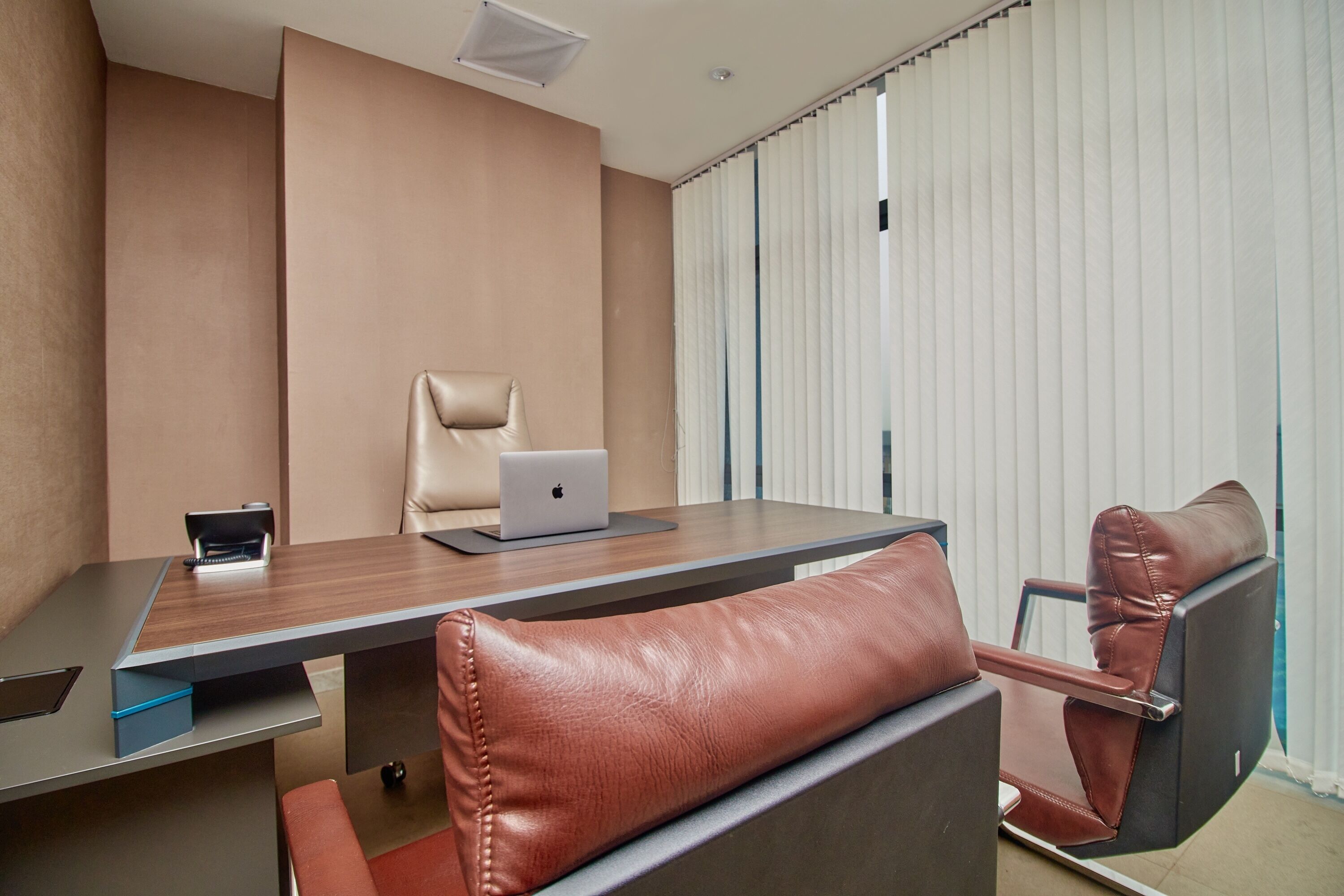 Una sala de conferencias con una mesa de madera, sillas de cuero, una computadora portátil y una ventana con persianas.