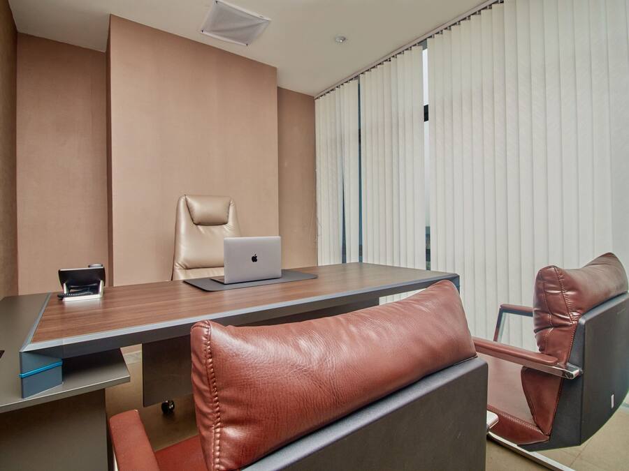 Una sala de conferencias con una mesa de madera, sillas de cuero, una computadora portátil y una ventana con persianas.