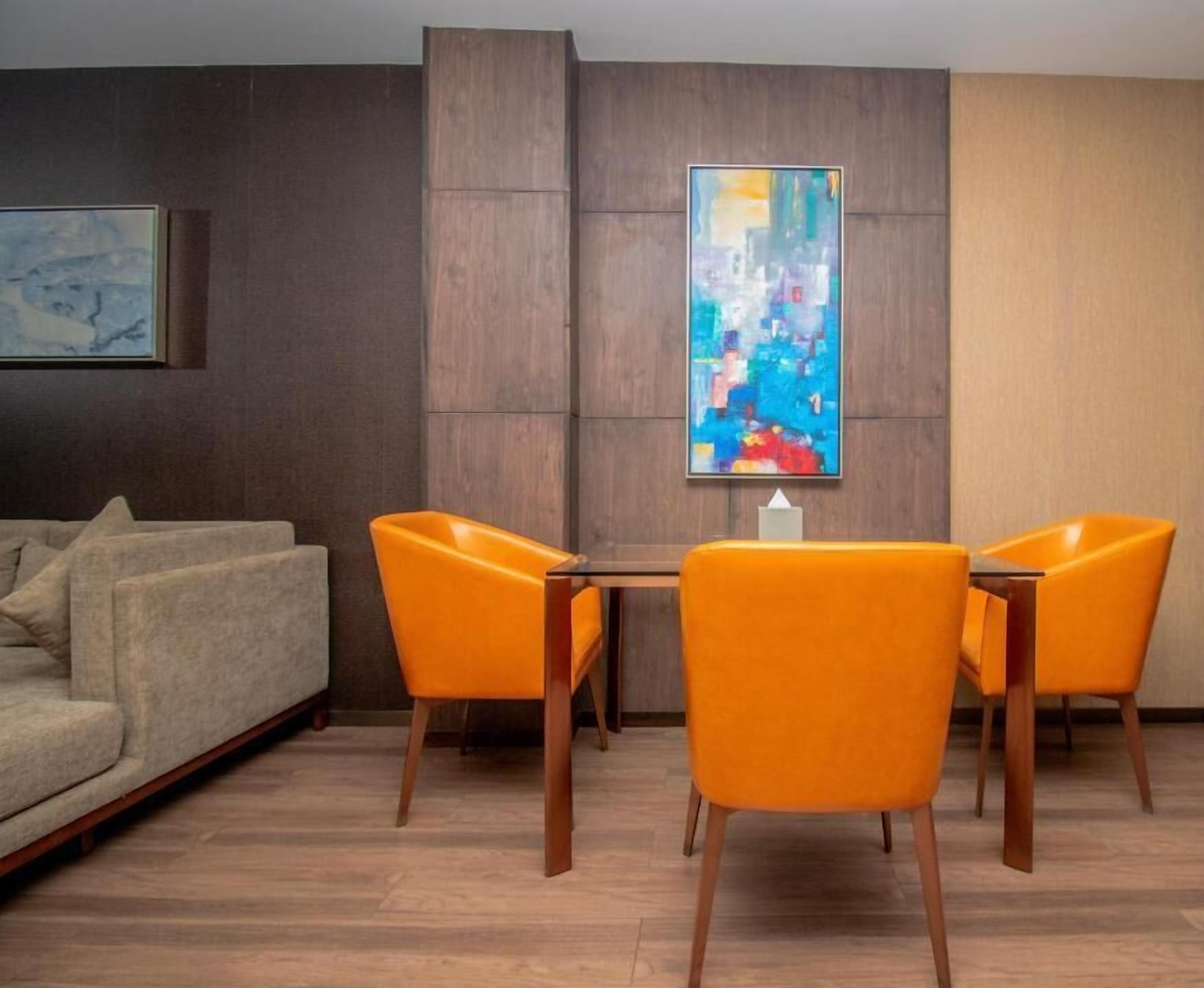 Een moderne kamer met een houten vloer, een beige bank en twee oranje fauteuils rond een klein tafeltje.