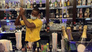 A bar area with a bartender preparing drinks, shelves of various liquor bottles, and glasses on the counter. - CIKA Golden Hotel and Suites (Lomé)