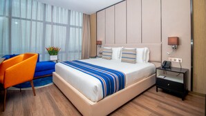 A hotel room with a large bed, a nightstand, a chair, and a window with curtains. - CIKA Golden Hotel and Suites (Lomé)