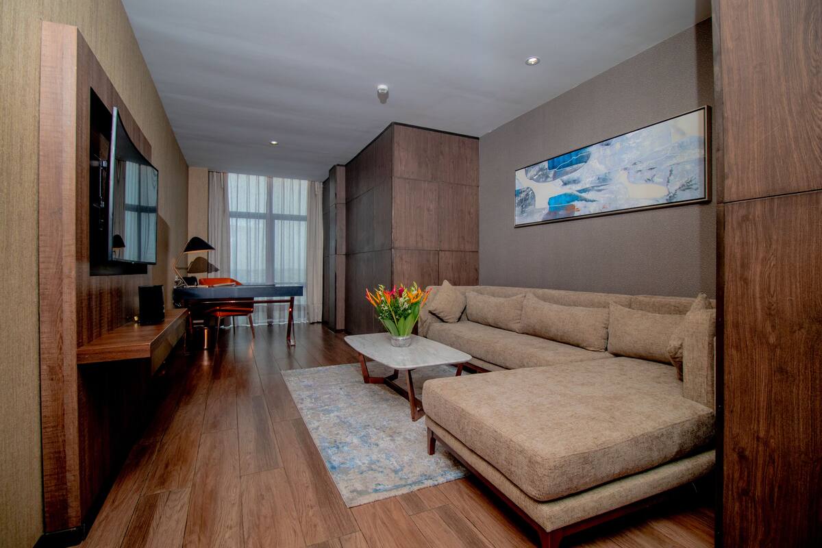 Uma sala de estar moderna com um sofá seccional, uma TV de tela plana, uma mesa de jantar e uma mesa de centro com flores.