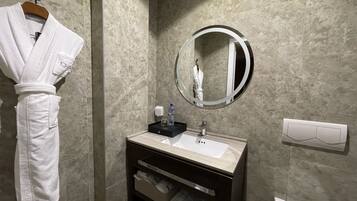 A bathroom with a marble wall, a round mirror, a sink, and a robe hanging on a rack.
