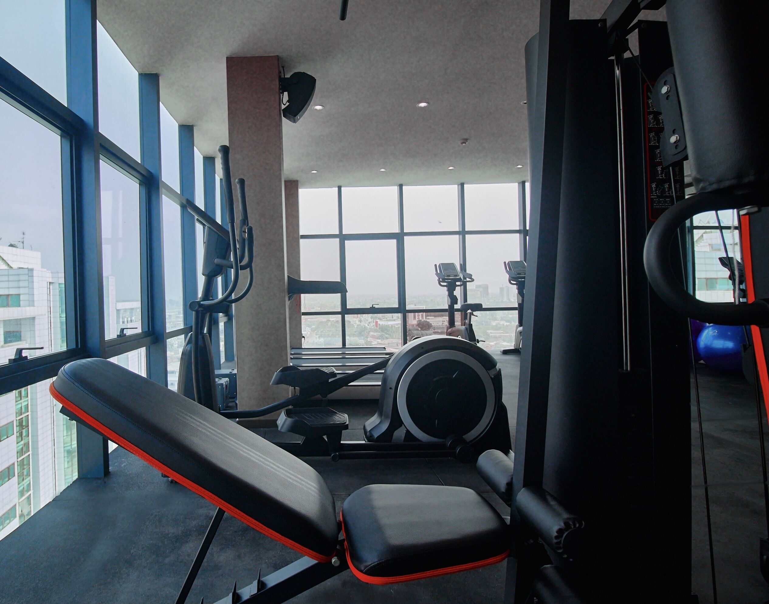 Un gimnasio con equipo de ejercicio, ventanas amplias y vistas de la ciudad.