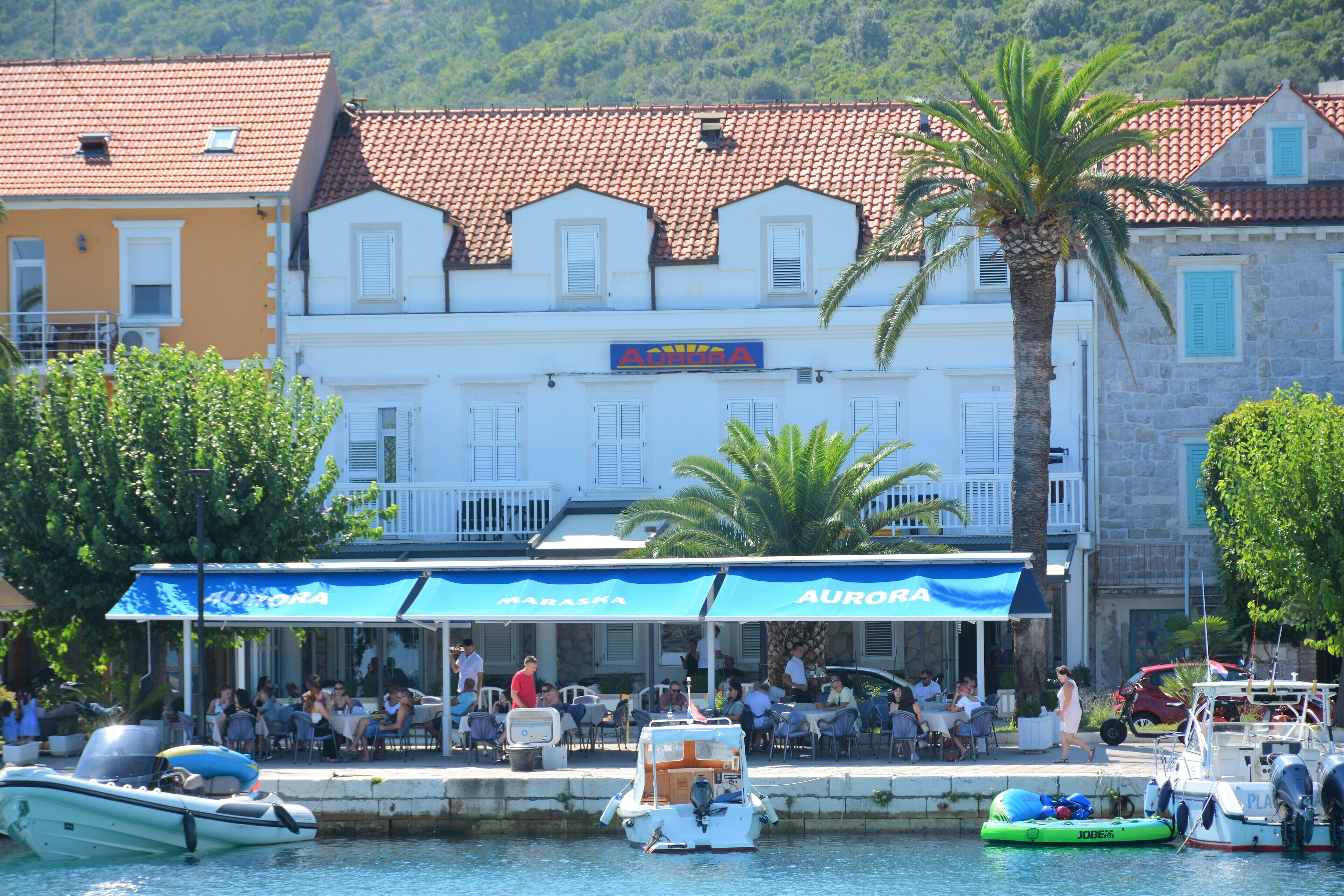 Un restaurant situé au bord de l’eau, avec une terrasse, un espace aménagé près de la piscine et des bateaux.
