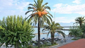 A coastal view with a palm tree, outdoor seating area, and a clear sky. - Guesthouse Aurora - Double Room with Sea View - 3 (Trpanj)