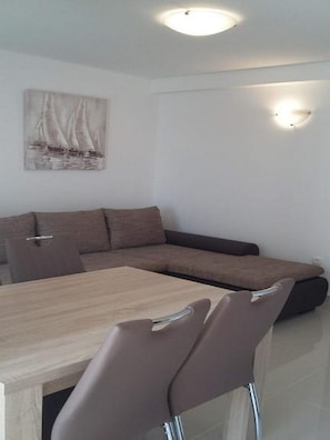 A modern living room with a wooden dining table, a brown sofa, and a painting of sailboats on the wall.