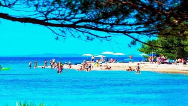 Une scène de plage avec des gens qui prennent un bain de soleil et se baignent, des parasols et un ciel bleu dégagé.
