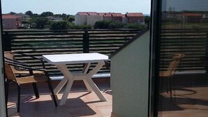 Un balcon avec une table et des chaises, une porte vitrée et une vue sur des bâtiments au loin.