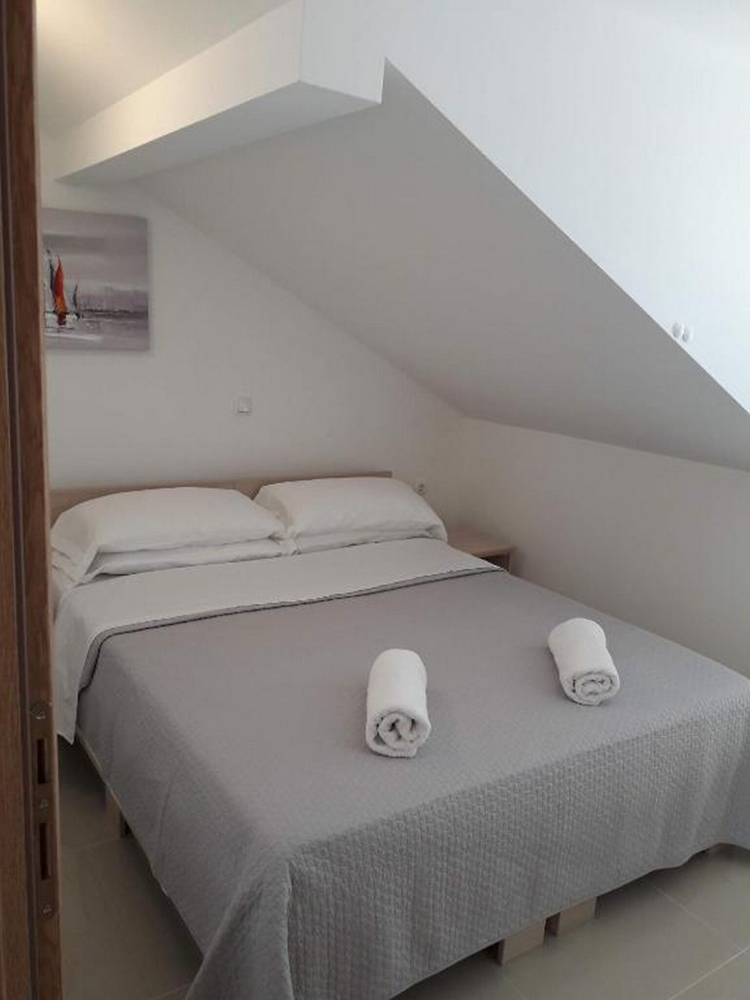 A single bed with a grey bedspread and two rolled towels.
