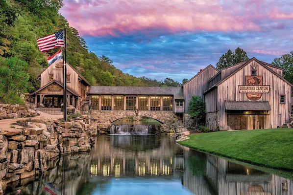 A rustic building with a sign reading "Dogwood Canyon Nature Park" and a stone bridge over a reflective water feature.