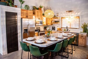 A modern kitchen with wooden cabinets, stainless steel appliances, and a central island with green chairs.