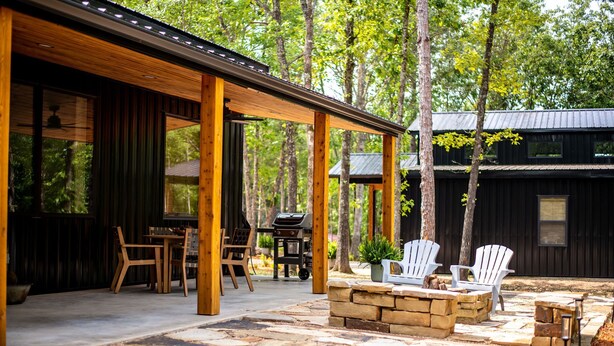 A covered patio with stone flooring, wooden furniture, and a grill area.