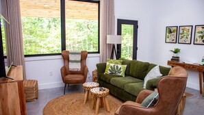 A modern living room with a green sofa, brown armchairs, a round woven rug, and a wooden side table with a lamp.