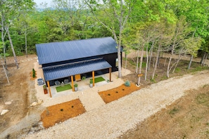 A two-story building with a dark roof, surrounded by trees and a gravel driveway.