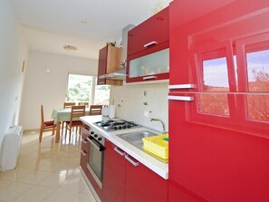 Une cuisine avec des meubles de rangement rouges, une cuisinière à gaz, un évier et un coin repas comprenant une table et des chaises.