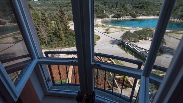 Vista desde una ventana a un paisaje costero con una señal de stop, árboles y cielo despejado.