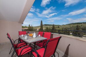 Un balcon avec une table dressée pour deux personnes, agrémenté de chaises rouges et d’une nappe blanche.
