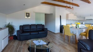 Una sala de estar moderna con un sofá negro, una mesa de centro de vidrio y un comedor con sillas amarillas.