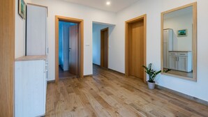 Un pasillo con suelo de madera, paredes blancas y puertas de madera. Hay una planta en maceta y un espejo en la pared.