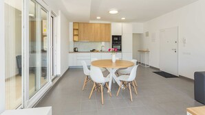 A modern kitchen with white cabinets, a wooden dining table with white chairs, and a built-in oven. - Villa Frida - Apartment Fran with Terrace (Premantura)