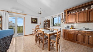 Un vaste espace de salle à manger avec une grande table et des chaises, une cuisine dotée de meubles en bois et une vue dégagée grâce aux portes vitrées.
