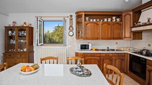 Une cuisine avec des meubles en bois, une table à manger ornée de fruits, un four à micro-ondes et une vue sur l’extérieur.