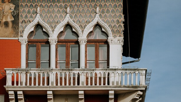 Une façade d’immeuble ornée de fenêtres de style gothique et dotée d’un balcon avec des balustrades blanches.