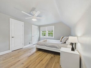 A bedroom with a bed, a nightstand, a ceiling fan, and a window with blinds.