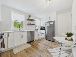 A modern kitchen with white cabinetry, a stainless steel refrigerator, and a dining area with a white table and chairs.