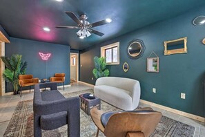 A modern living room with a ceiling fan, a neon sign, and a variety of seating options.