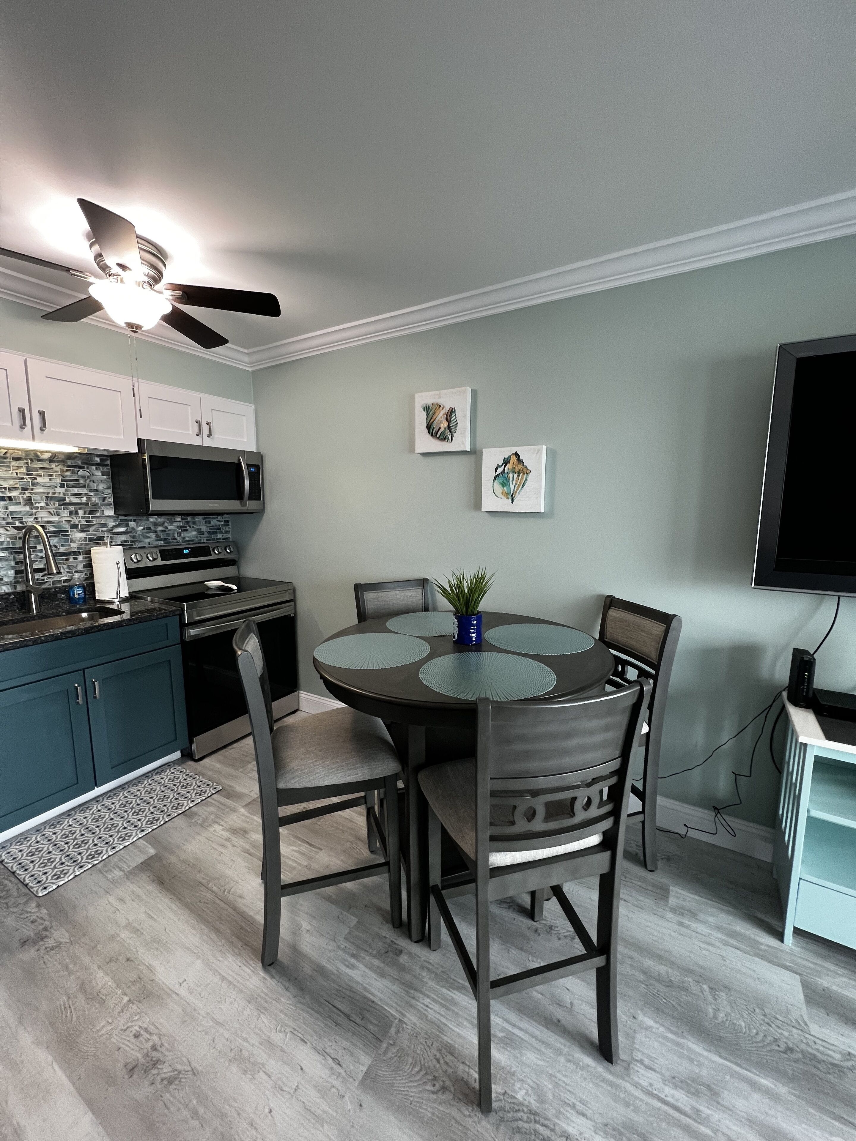 Une cuisine moderne avec des meubles de couleur sombre, un four à micro-ondes et un coin repas comprenant une table ronde et des chaises.