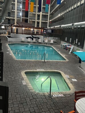 Un espace piscine intérieure comprenant deux piscines, des chaises longues et un coin salon.