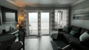 Ein modernes Wohnzimmer mit Flachbildfernseher, einem Esstisch mit Stühlen, einer Sofagarnitur und Meerblick durch große Fenster.
