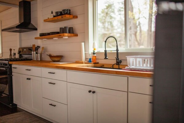 Una cocina moderna con armarios blancos, encimeras de madera, una campana extractora negra y un ventanal que proporciona luz natural.