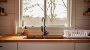 Une cuisine équipée d’un évier, d’un plan de travail en bois et d’une fenêtre donnant sur la forêt.