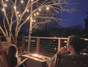 A deck with a fire feature and string lights, surrounded by trees.