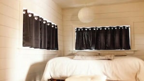 Une chambre à coucher avec un lit, un tabouret en bois et une fenêtre avec des rideaux noirs.